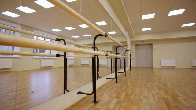 Wooden handrails installed near mirror wall in spacious ballet class. Empty classic dance studio interior lit by led lamps. Training gym