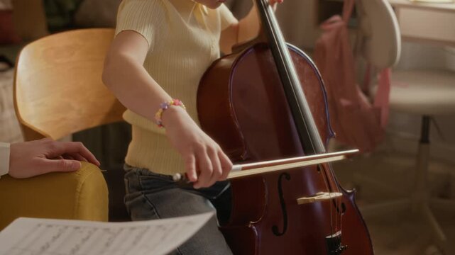 Tilt up shot of Caucasian girl playing cello with bow during music lesson at home with teacher holding sheet music. Video perfect for educational programs, music school promos, and tutoring services