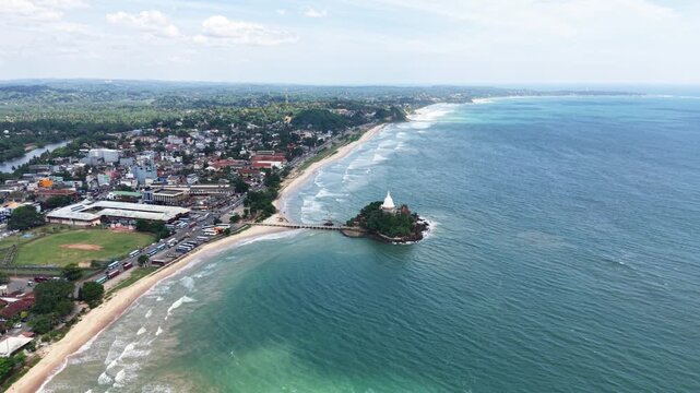 Aerial view of Parewi Duwa Temple on a small island connected by a bridge to the coastline of Matara, Sri Lanka.