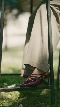 A stylish close-up shot captures a woman's foot adorned in elegant burgundy high-heeled shoes and wide-leg pants. This fashionable footwear detail is showcased in a serene outdoor setting