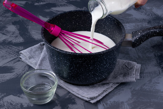 Milk is poured into a saucepan. Vinegar is in a glass bowl nearby on the gray table. Fresh cheese making step by step. Dairy production, coagulation