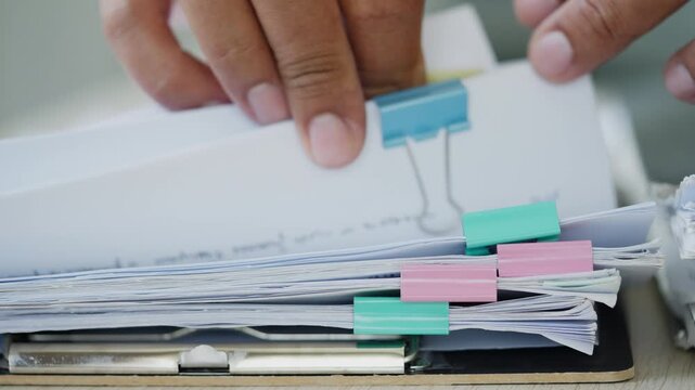 Close up of hands arranging document stacks on clipboard, showing office archive, file control, business records, compliance checking, paperwork overload, and administrative workflow.