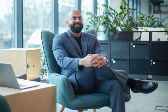 A man in a suit is sitting in a chair in front of a laptop