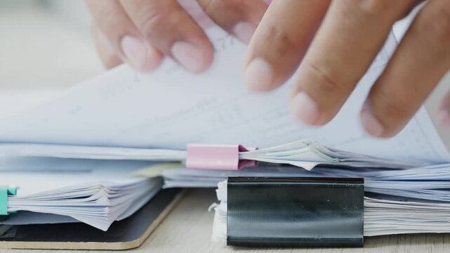 Adult office worker managing stacked documents beside binder clips, symbolizing document management, audit preparation, business records, approval process, and administrative workflow.