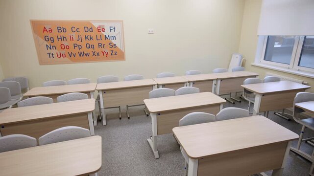 Desks with chairs rows and ABC placard in English class. Classroom for foreign language learning in modern school building interior