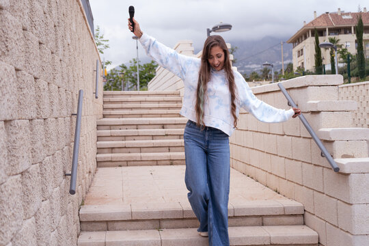 Young woman singing and dancing with microphone on stairs