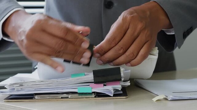 Business professional sorting thick paperwork with binder clips at office desk, representing document management, corporate filing, administrative workflow, audit records, and productivity.
