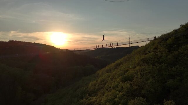 Highline Aerial Shot. Brave Girl Tightrope Walker is on a rope stretched between Mountains at high altitude, Sunset Time