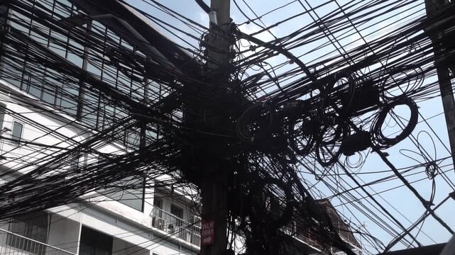Messy power wires are tangled on the electrical pole, creating a chaotic arrangement of internet cables and powerlines in Thailand.