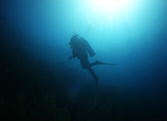 Fototapeta premium Scuba diver silhouette ascending toward dramatic sunburst in deep blue ocean