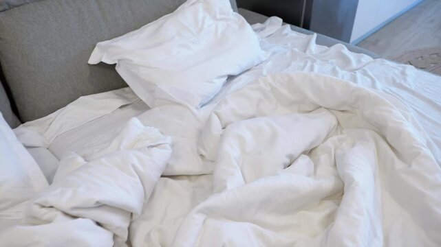 Unmade bed with white rumpled linens. Close-up view of a messy unmade bed with crumpled white sheets, duvet, and pillows in a modern bedroom, suggesting a comfortable and lazy morning at home