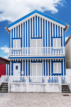 Iconic wooden house with colorful vertical stripes under a clear blue sky in Costa Nova, Portugal.