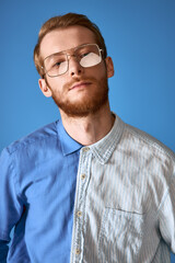 Obraz premium Red haired man showcases modern fashion with unique style against a vibrant blue backdrop.
