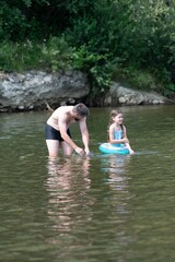 Fototapeta premium A father and daughter enjoy a summer day playing in a river. The girl is using a small inflatable ring.