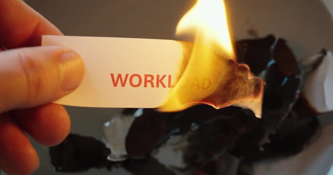 Close-up of a paper note with the word workload burning in a flame, symbolizing job stress, burnout, pressure, overwork, and emotional release.