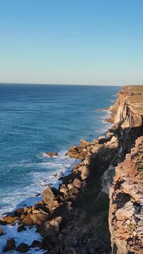 Vertical drone shot flying along the Bunda Cliffs in the morning light, gradually approaching the sheer cliff face