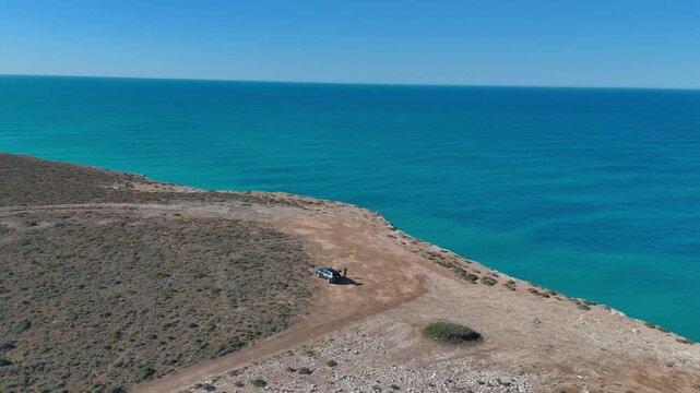 Drone shot orbiting a parked car near the Bunda Cliffs, with deep blue ocean and sky stretching to the horizon
