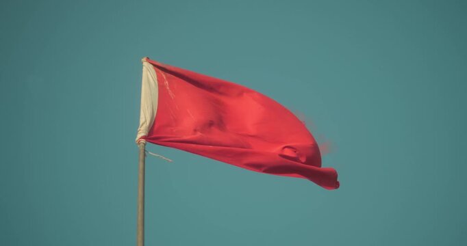 Red flag blowing strongly in the wind against a clear blue sky, close-up view