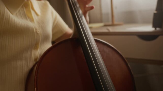 Handheld shot of child practicing cello during music lesson at home, focusing on finger placement and bow technique. Clip is ideal for promoting youth music schools and private tutoring services