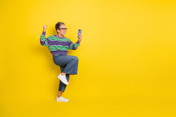 Obraz premium Joyful mature woman in striped sweater poses with phone against bright yellow background