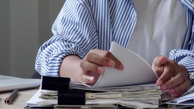 Female administrative worker organizing paper files with binder clip on office desk, highlighting document management, business records, archive storage, corporate workflow, and compliance review.