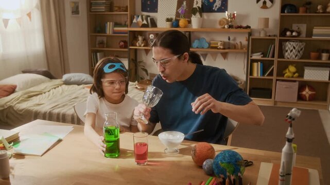 Asian young father and multiethnic child conducting chemistry experiment at home, pouring colorful liquids. Video perfect for promoting STEM education, homeschooling, and family learning