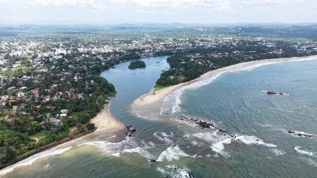 Aerial view of the Nilwala River mouth meeting the Indian Ocean with sandy beaches and lush coastal vegetation in Matara, Southern Province, Sri Lanka.