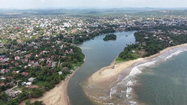 Aerial view of the Nilwala River mouth meeting the Indian Ocean with a sandy beach and coastal town in Matara, Southern Province, Sri Lanka.