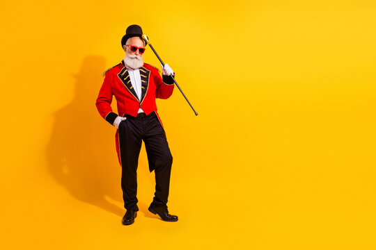 Circus magician in red tail coat with top hat and cane poses on a vibrant yellow background