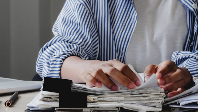 Hands gently flip through stacked newspapers. Person wears striped shirt, focused on reading. Scene suggests quiet, thoughtful research or news consumption. Useful for articles, business reports