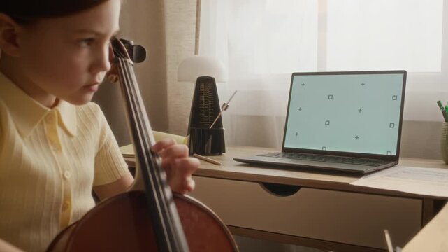 Handheld shot of Caucasian child practicing cello in front of laptop with blank screen mockup. Clip is ideal for marketing online music tutoring, remote education, and e-learning apps