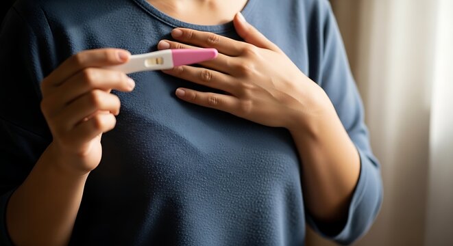 ​A woman holding a pink home pregnancy test to her chest, expressing deep emotion in soft window light.