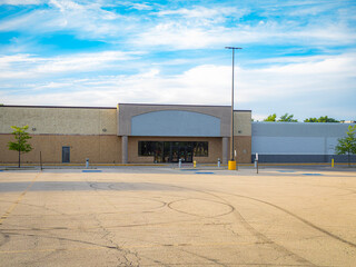 Fototapeta premium Wide shot of an abandoned empty big box retail store building with a blank sign facade and a vacant asphalt parking lot under a blue sky