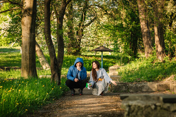 Fototapeta premium Happy couple crouching and posing on a path in a sunny spring park. Man and a woman enjoying nature together. Mom and dad are sitting and watching their children play off-screen.