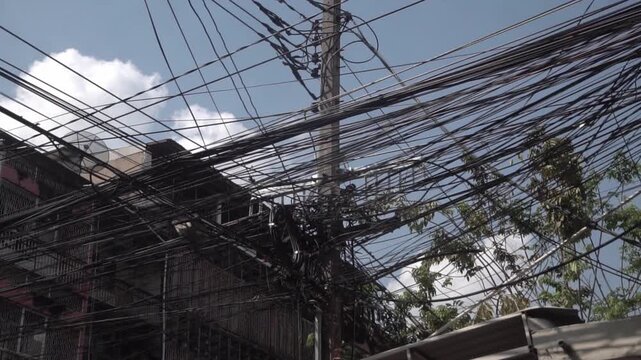 Messy power wires are tangled on the electrical pole, creating a chaotic arrangement of internet cables and powerlines in Thailand.