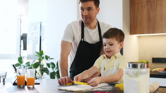 Father and son engage in baking activity in a contemporary kitchen, with flour on the countertop and orange juice glasses placed beside them