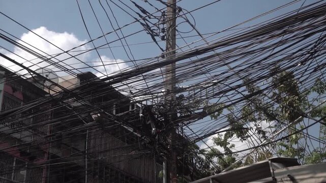 Messy power wires are tangled on the electrical pole, creating a chaotic arrangement of internet cables and powerlines in Thailand.