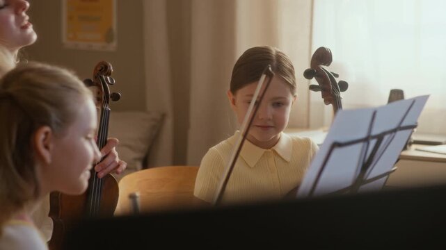 Tilt up shot of female teacher explaining music theory to Caucasian children holding flute and cello during home lesson. Video perfect for promoting private tutoring and music education programs