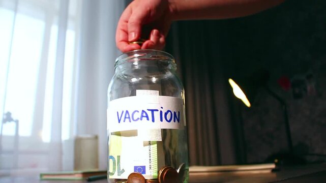 Close up of transparent money jar labeled for VACATION. Represents traditional saving methods and conscious money management for future