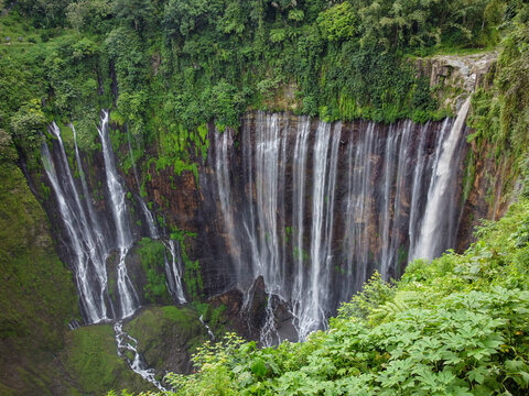 Drone view of Tumpak Sewu Waterfall cascading through a steep canyon surrounded by dense tropical vegetation in East Java, Indonesia.