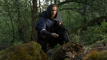 Fototapeta premium Mysterious hooded figure explores a lush, mossy forest floor.