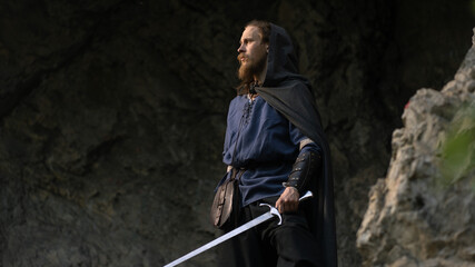 A rugged warrior stands poised with a sword, gazing into a shadowy wilderness. © horimono