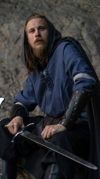 A rugged warrior with a sword and shield stands ready against a rocky backdrop.