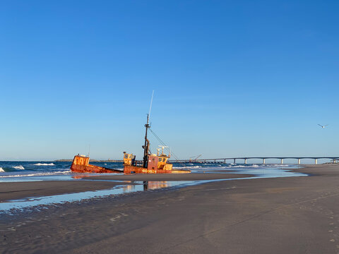 Abandoned shipwreck on a wide sandy beach in the Outer Banks of North Carolina, with ocean waves, distant bridge, and expansive blue sky.