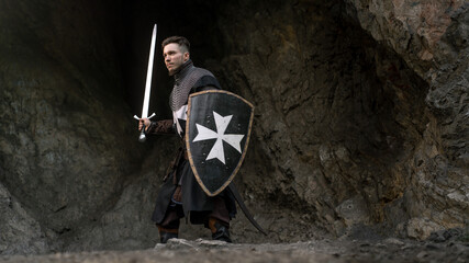 Knight stands ready with sword and shield against a rocky backdrop. © horimono
