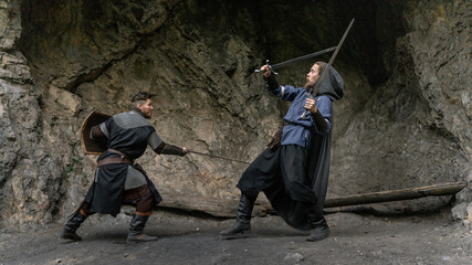 Fototapeta premium Two warriors clash swords amidst a rocky, cavernous setting.