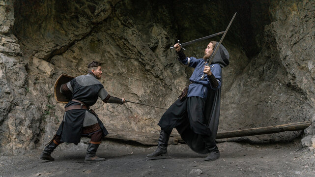 Two warriors clash swords amidst a rocky, cavernous setting.