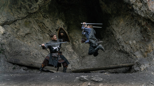Medieval warriors clash amidst a rocky cavern, swords raised in dynamic action.