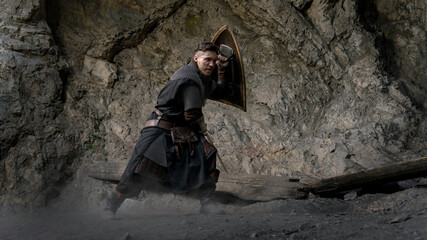 A warrior with a shield and sword stands ready amidst rocky terrain, poised for battle. © horimono