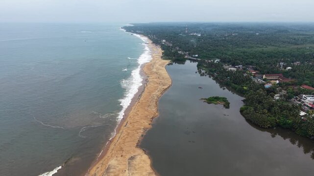 Aerial view of Mahamodara Lake separated from the ocean by a narrow sandy beach with lush tropical vegetation and buildings in Galle, Southern Province, Sri Lanka.